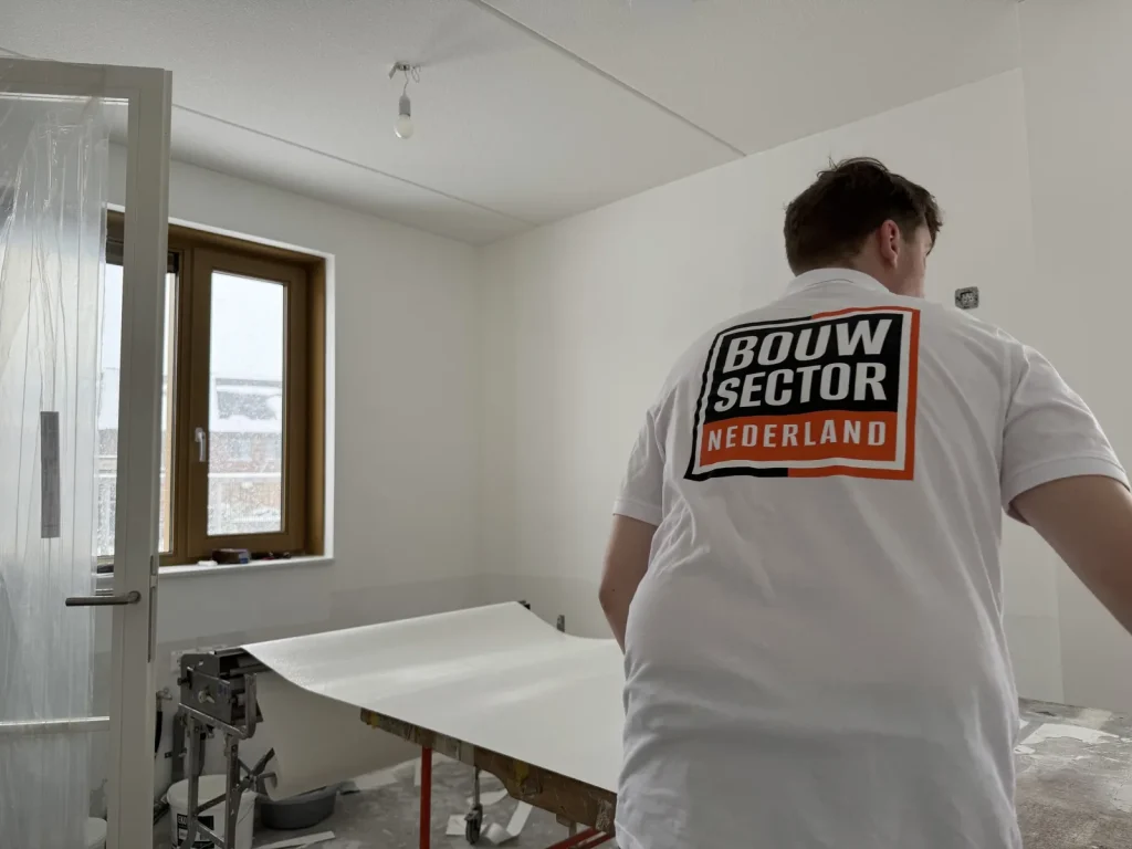 Behanger in een wit shirt van Bouwsector Nederland trekt een baan van de plaktafel in een lege kamer