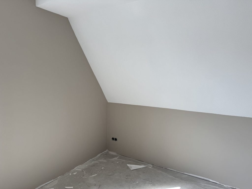Zolderkamer in een nieuw huis met een schuine wand en egaal afgewerkte muren in een warme grijstint
