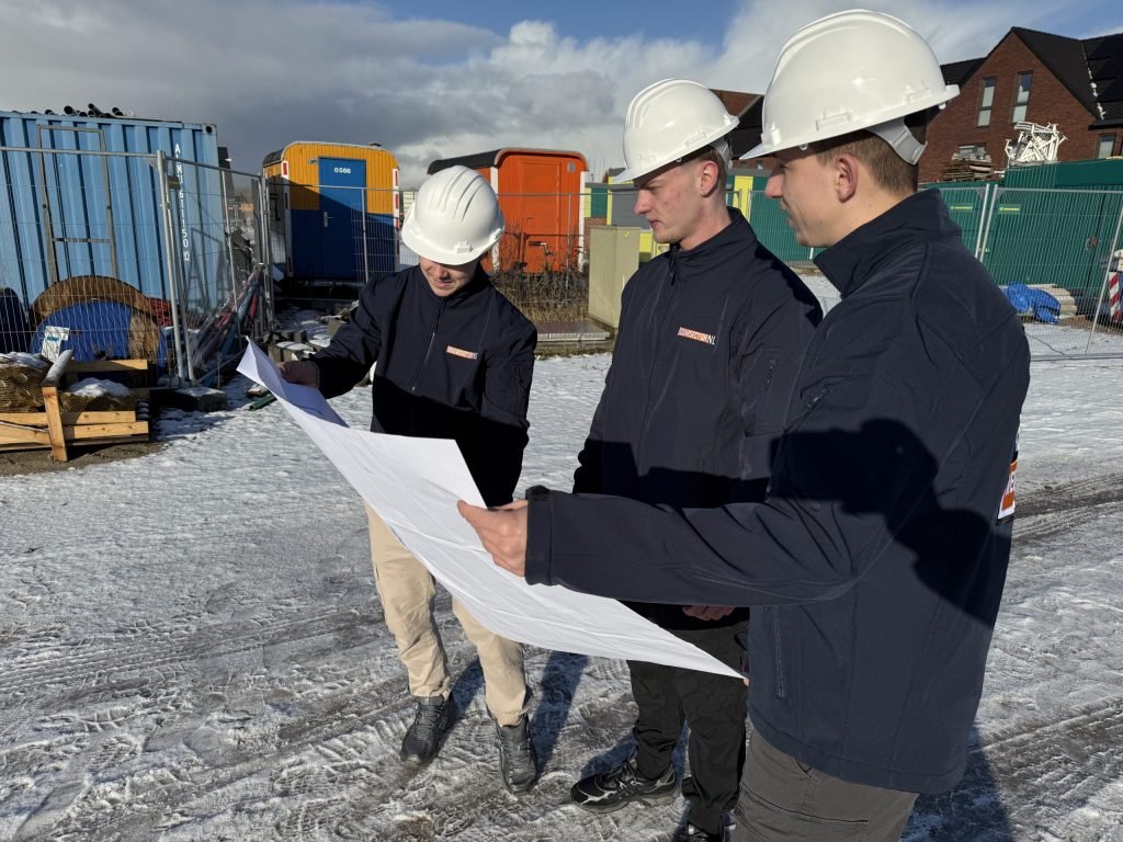 Drie medewerkers van Bouwsector Nederland met witte helm bekijken samen een bouwtekening op de bouwplaats